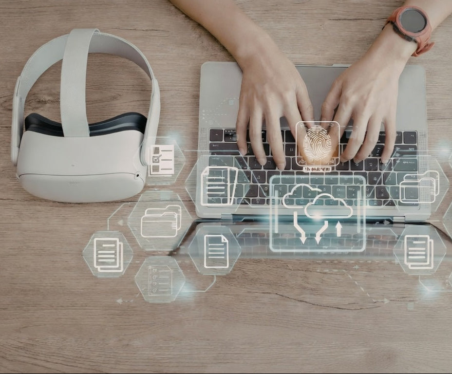 Person using a laptop with a VR headset and smartphone on a wooden table.